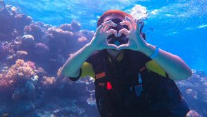 A girl in scuba diving near a sea reef, shows a heart with her hands