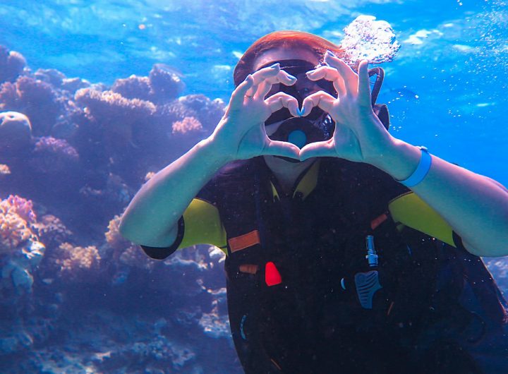 A girl in scuba diving near a sea reef, shows a heart with her hands